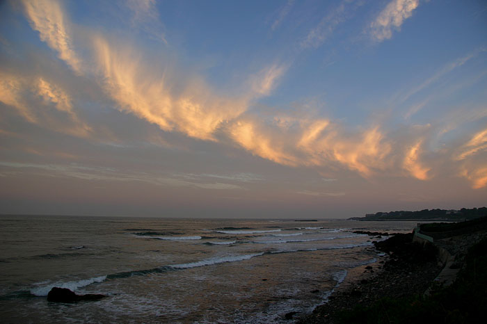 As the evening sun sets, it casts a peachy glow across whispy cirrus clouds that mimic the cresting ocean waves below.
